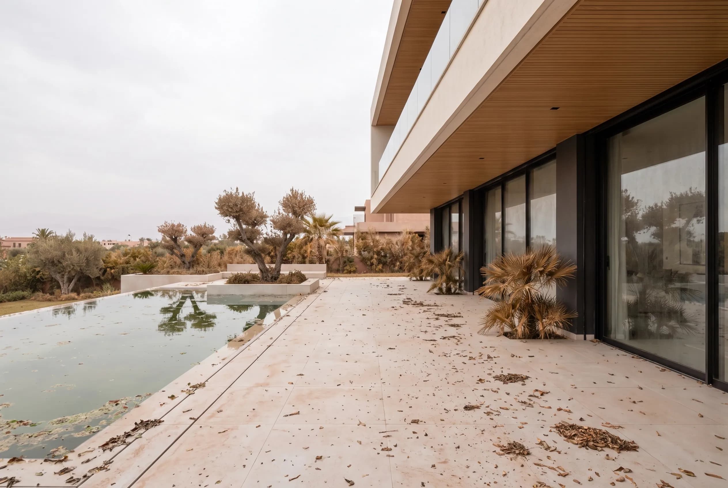 The villa exterior after months unattended — dulled terrace, tired planting, cloudy pool edge