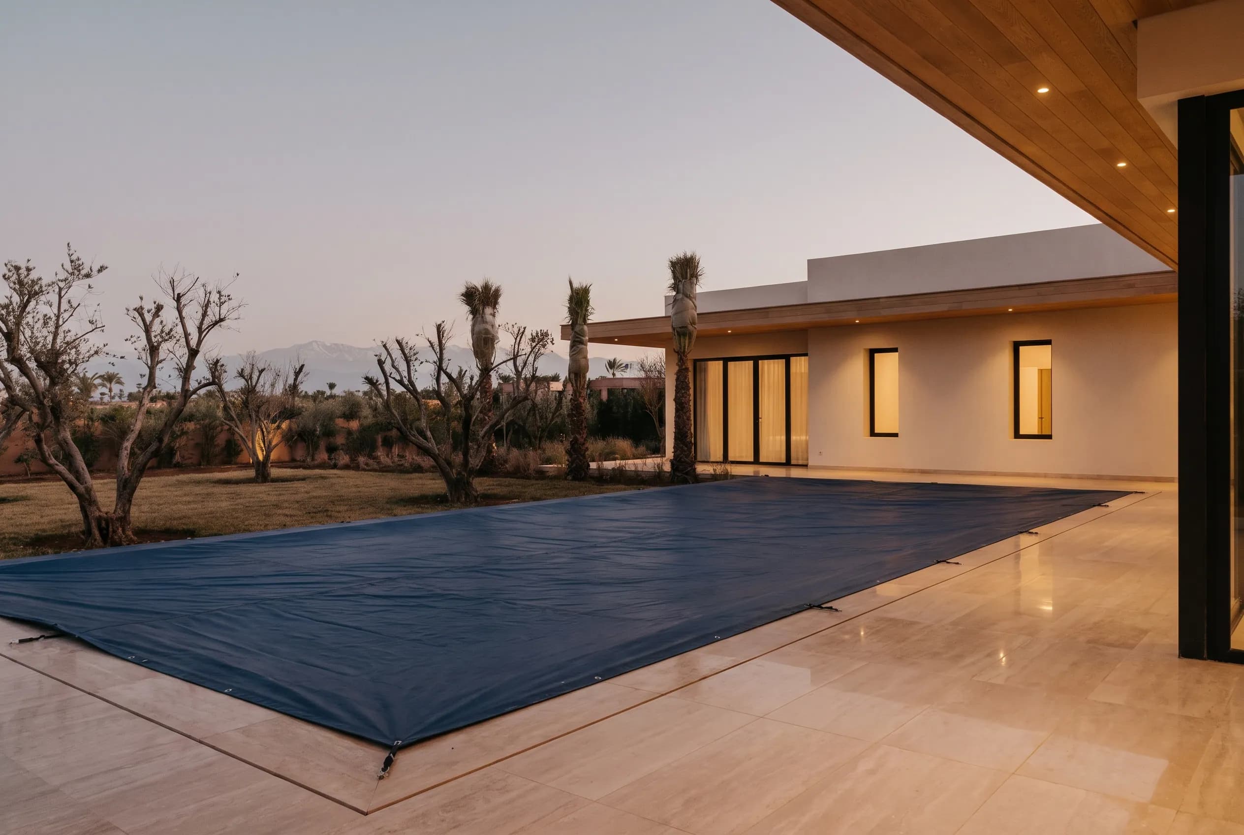 Pool under a taut winter cover at dusk, villa lights warm beyond